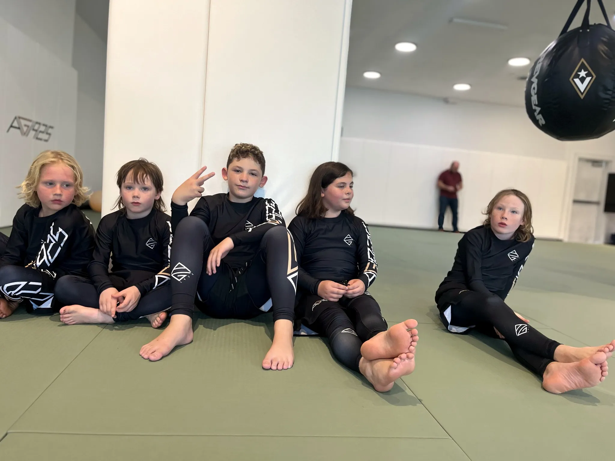 Kids in AG1925 rashguards and spats sitting along the academy wall